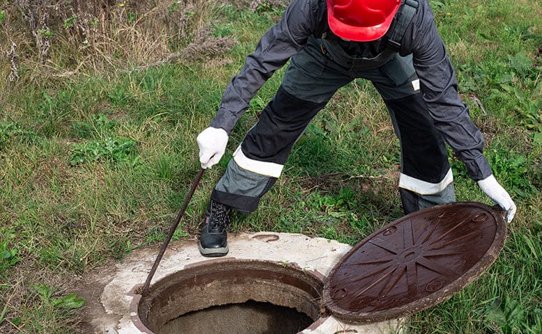 A plumber lifting a manhole and inspecting a sewage line.